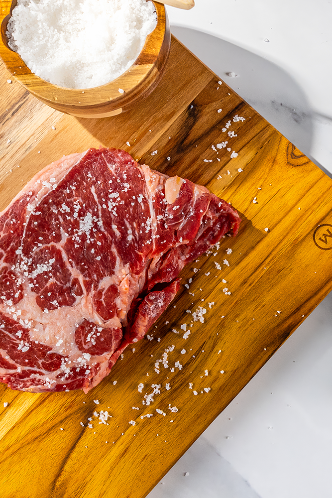 Raw steak on a wooden cutting board with natural grain Baja Gold mineral sea salt sprinkled on top.